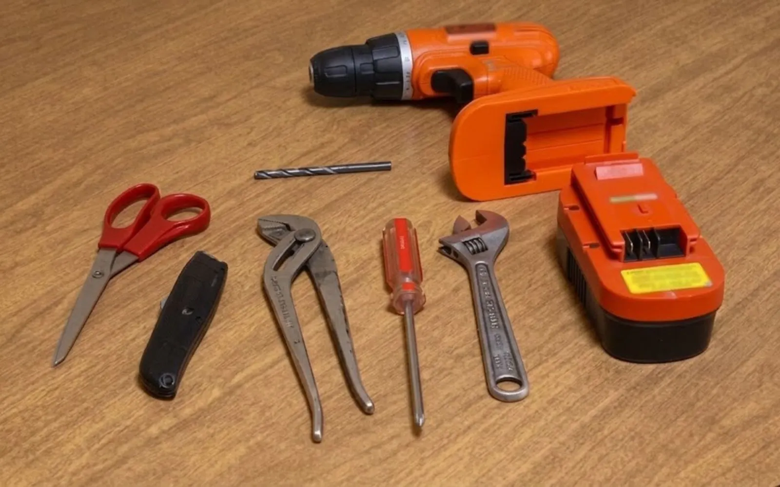 Plumbing hand tools and a cordless drill laid out on a workbench