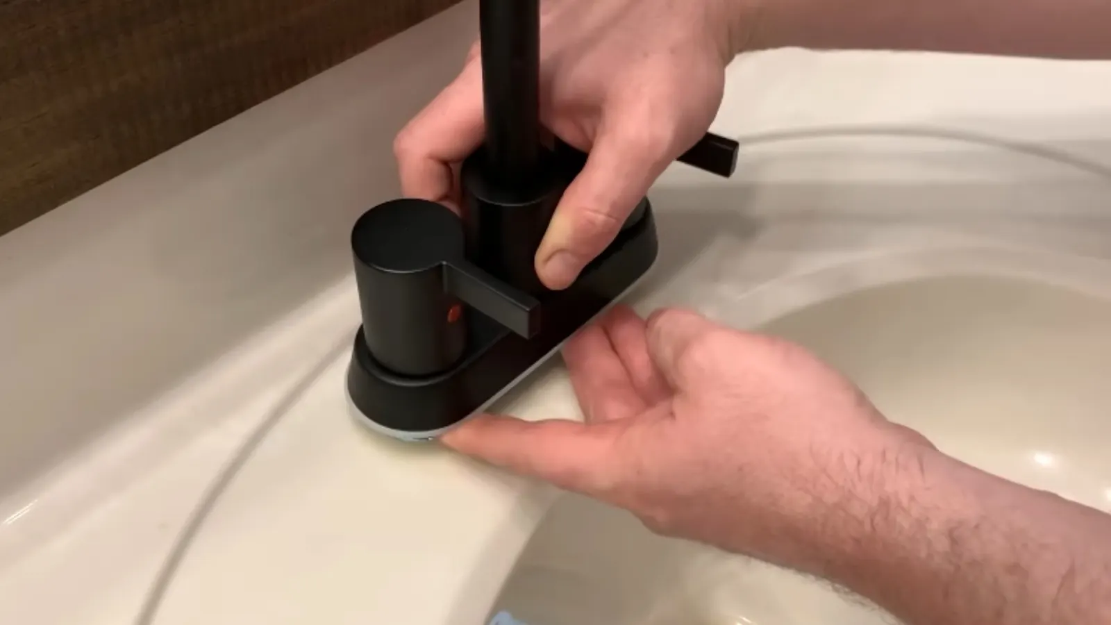 Hands installing a new black faucet on a white bathroom sink