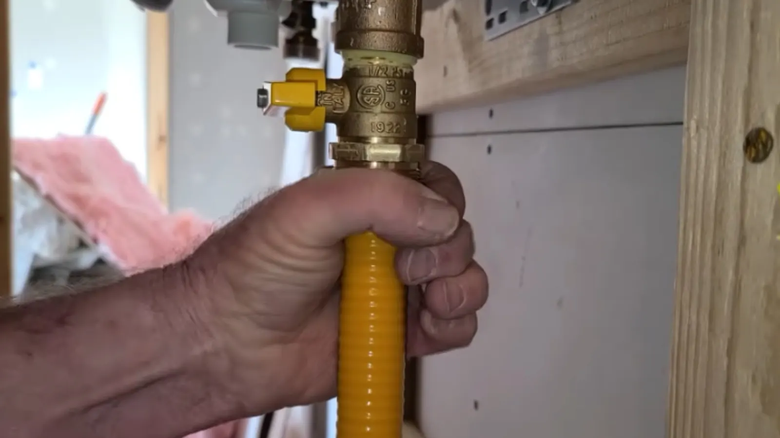 Hand tightening a yellow coated flexible gas line at a brass shutoff valve