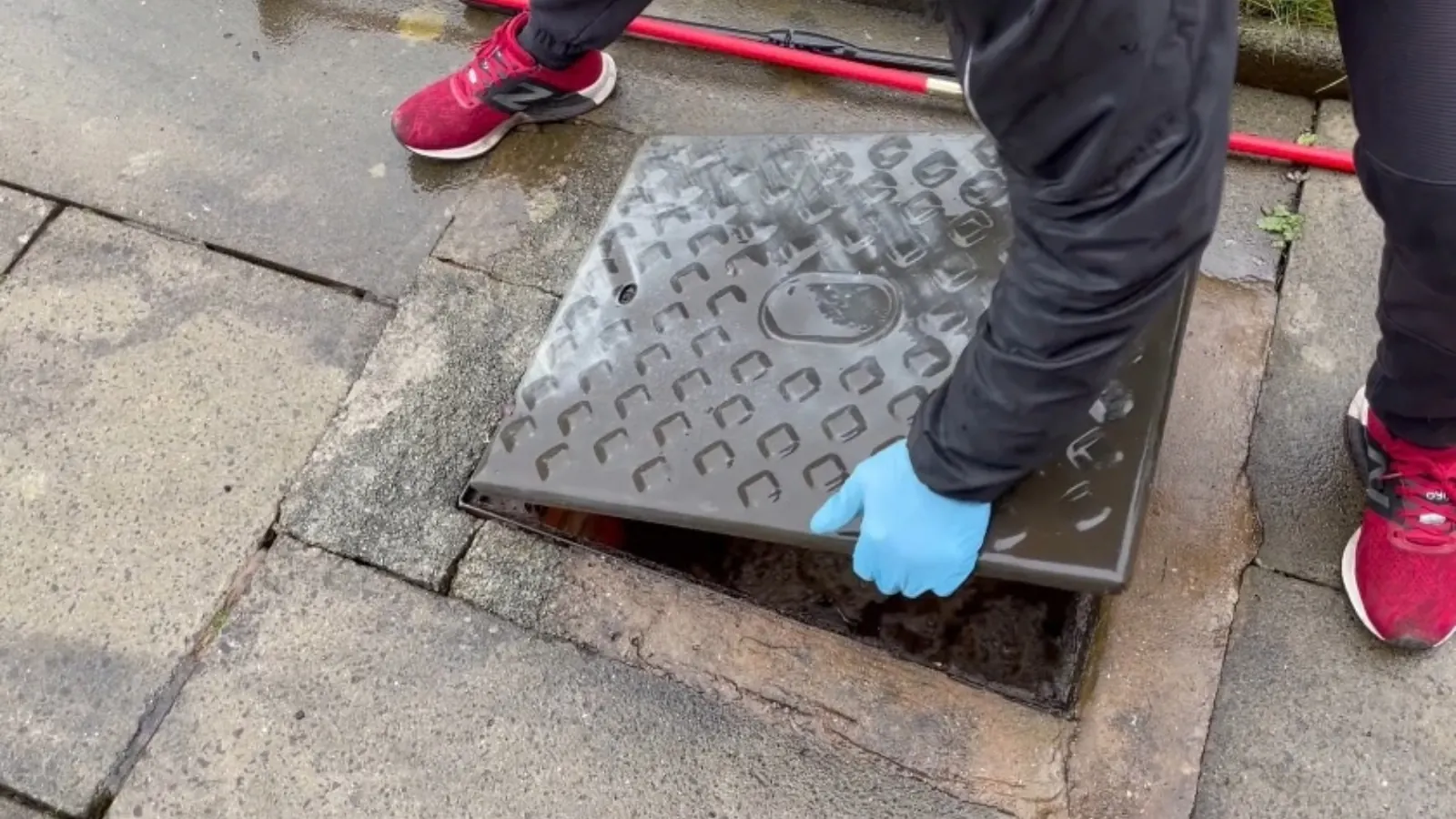 Gloved hand lifting an access cover to reach a backed-up sewer line