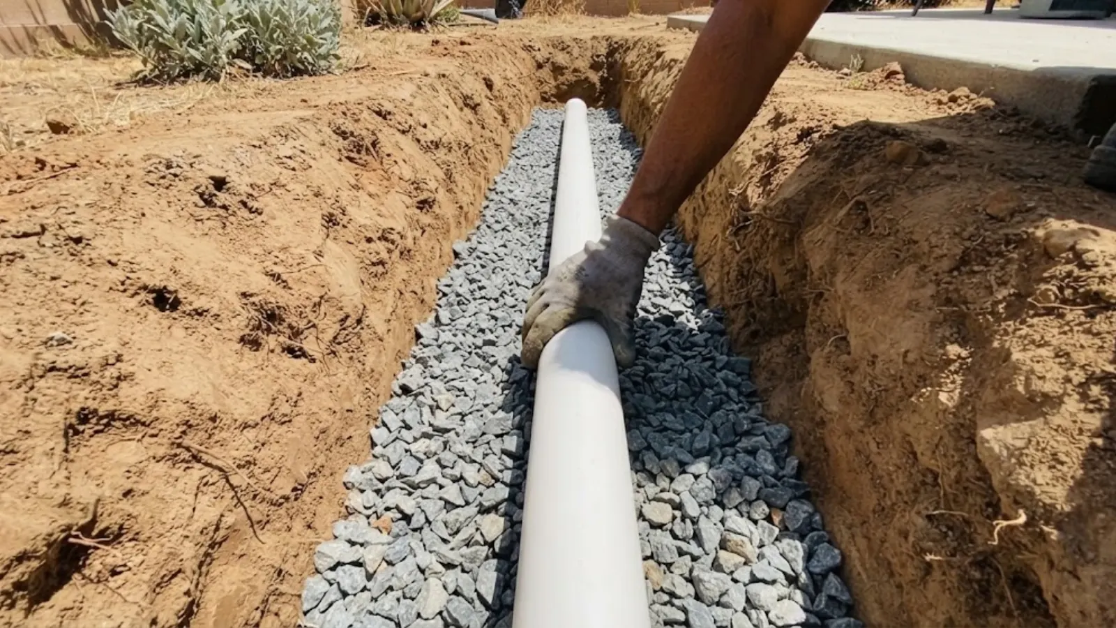 New PVC sewer line laid on gravel bedding in a trench beside a home