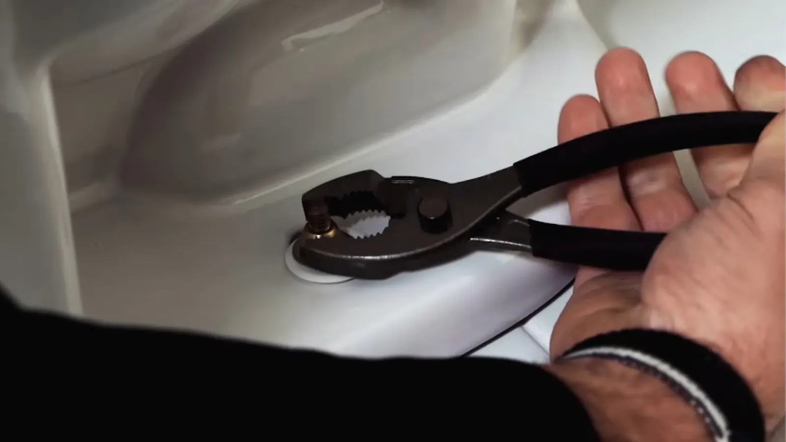 Hand using pliers on a toilet supply fitting during a repair