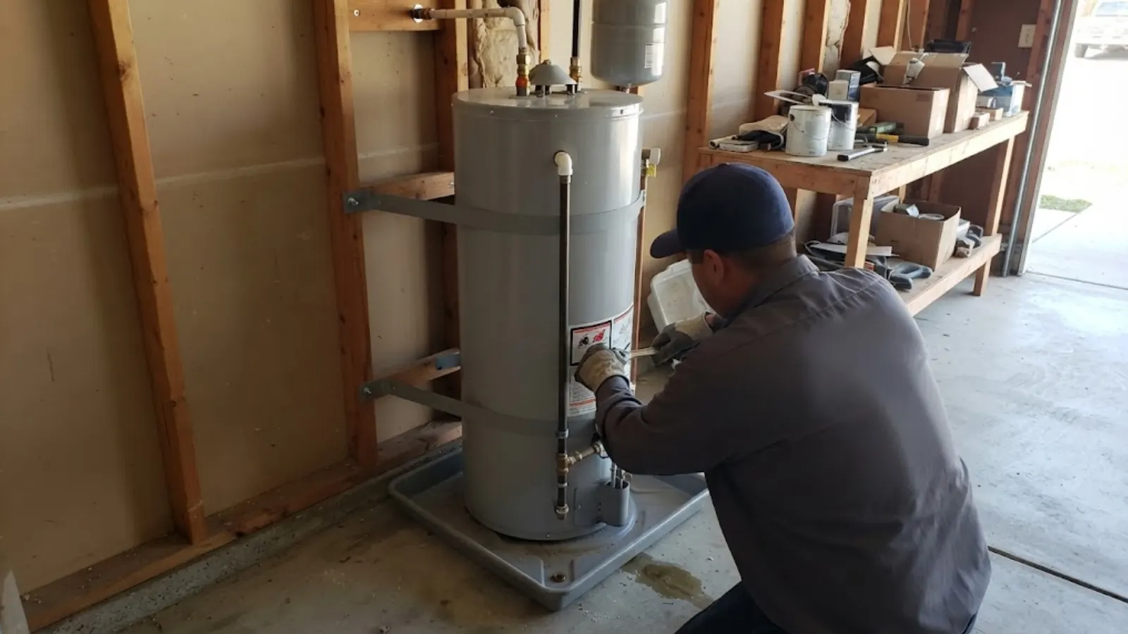 Plumber installing a new tank water heater on a stand in a Costa Mesa garage